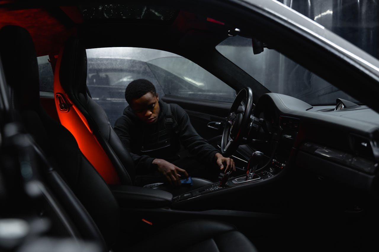 A man carefully cleaning the interior of a car at night, focusing on detailing.